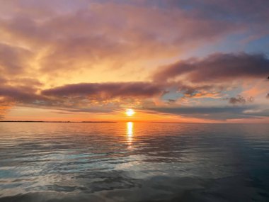   Deniz batımında güzel bir gün batımı pembe altın sarısı bulutlar üzerinde mavi mavi gökyüzü yarı akşam, su dalgası doğa manzarası yansıması