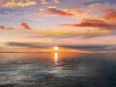   Deniz batımında güzel bir gün batımı pembe altın sarısı bulutlar üzerinde mavi mavi gökyüzü yarı akşam, su dalgası doğa manzarası yansıması