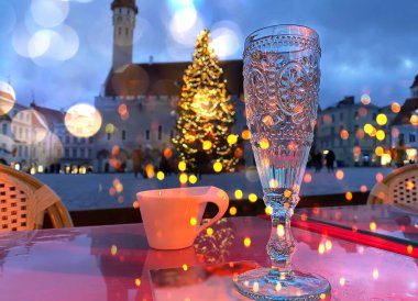 Kasaba meydanındaki kafeterya masasındaki Noel ağacında bir bardak şampanya ve bir fincan kahveyle insanlar kış tatilini kutluyor.
