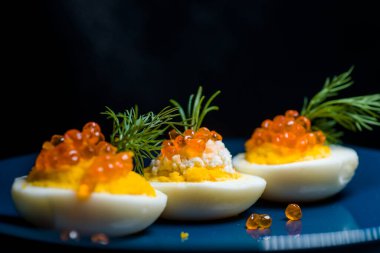 Kırmızı havyarla doldurulmuş yumurtalar lezzetli ve sağlıklı. Bir restoranda mavi tabakta servis edilen Paskalya için en iyi yemek.