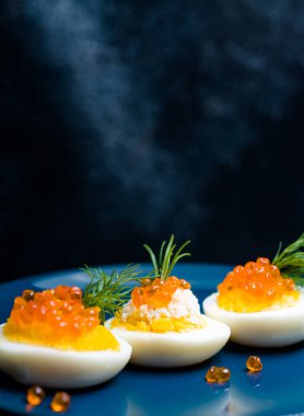 Kırmızı havyarla doldurulmuş yumurtalar lezzetli ve sağlıklı. Bir restoranda mavi tabakta servis edilen Paskalya için en iyi yemek.