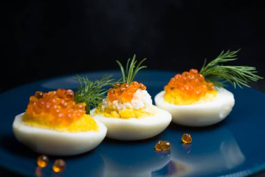 Kırmızı havyarla doldurulmuş yumurtalar lezzetli ve sağlıklı. Bir restoranda mavi tabakta servis edilen Paskalya için en iyi yemek.