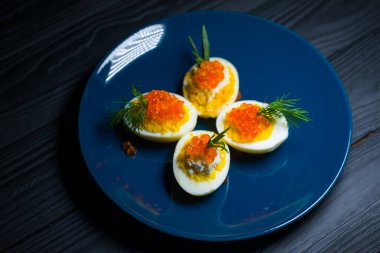 Kırmızı havyarla doldurulmuş yumurtalar lezzetli ve sağlıklı. Bir restoranda mavi tabakta servis edilen Paskalya için en iyi yemek.