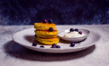 Beyaz bir tabakta peynir ve undan yapılmış küçük gözlemeler. Mavi arka planda lezzetli yemekler var.