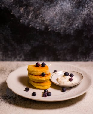 Beyaz bir tabakta peynir ve undan yapılmış küçük gözlemeler. Mavi arka planda lezzetli yemekler var.