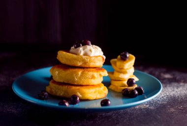 Küçük, kalın bir krep, böğürtlenli ve ekşi kremalı, güzel mavi bir tabakta.