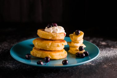 Küçük, kalın bir krep, böğürtlenli ve ekşi kremalı, güzel mavi bir tabakta.