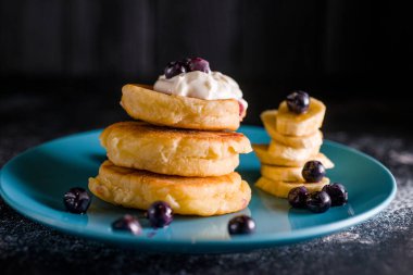 Küçük, kalın bir krep, böğürtlenli ve ekşi kremalı, güzel mavi bir tabakta.