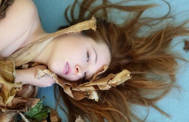 Uzun kızıl saçlı seksi bir kadının güzel şehvetli portresi kurumuş, kurumuş muz ağacının yaprakları arasında sanatsal bir şekilde süslenmiş.