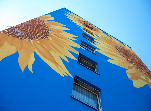 Sanatsal olarak boyanmış bir evin parçası, gökdelen gökyüzüne uzanıyor, mavi evin duvarlarında, pencerelerinde, duvar resimlerinde, kopya alanlarında büyük ayçiçekleri var.