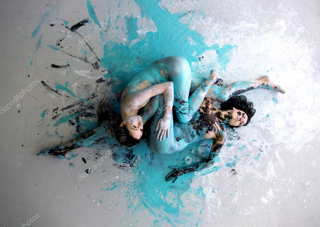 two white black and turquoise abstractly painted sexy young women on the floor, abstract body art painting.