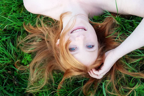 一个年轻美丽的性感红头发女人的笑脸画像 她把红头发展开成扇形 光秃秃的肩膀放松地躺在绿草上 倒挂着 复制着空间 — 图库照片