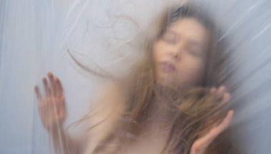 Bulanık, odak dışında güzel seksi şehvetli kadının portresi şeffaf plastik folyonun arkasında, arka plan olarak bir rüya gibi, kopyalama alanı