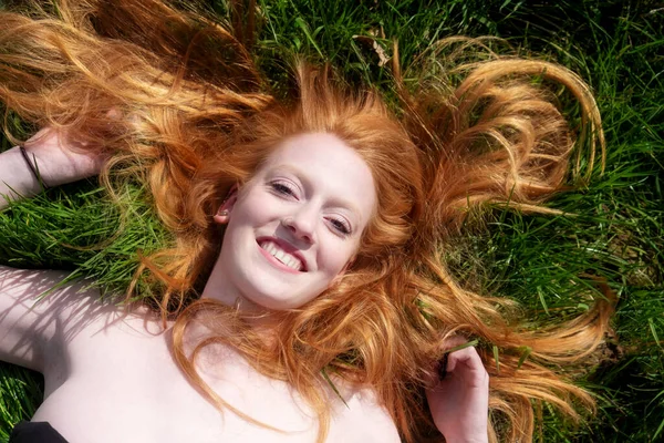 一个年轻性感的红头发女人的美丽画像 躺在春天 夏日的阳光下 悠闲地躺在绿茵的草地上 长长的红头发飘扬在头顶上 复制空间 — 图库照片