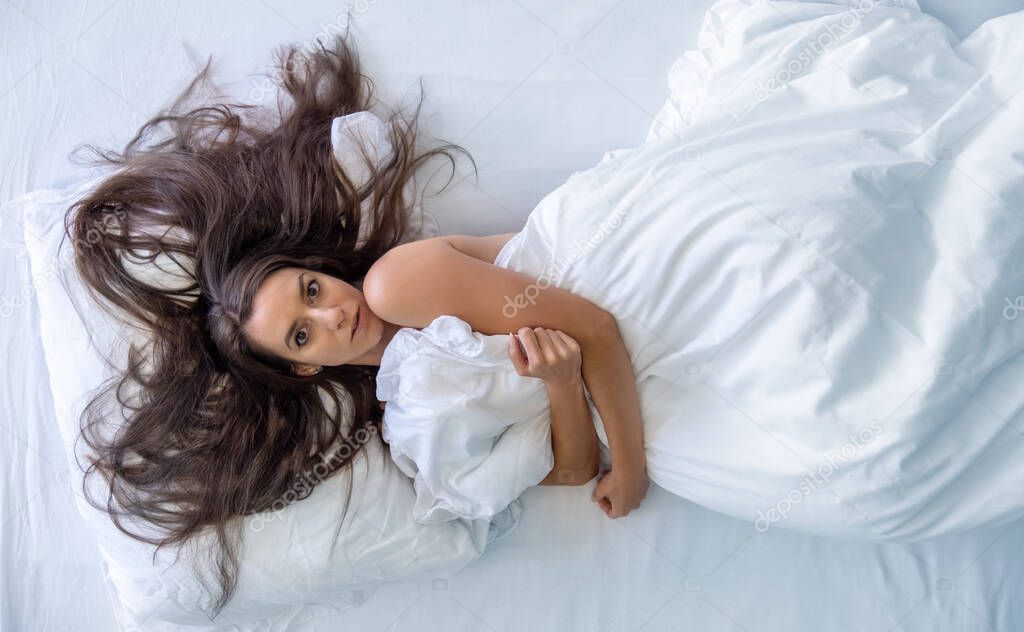 Top view from above to an attractive, young, sexy, wild, windblown, brunette, long haired, portrait of woman in bed hugging the bedspread, copy space.
