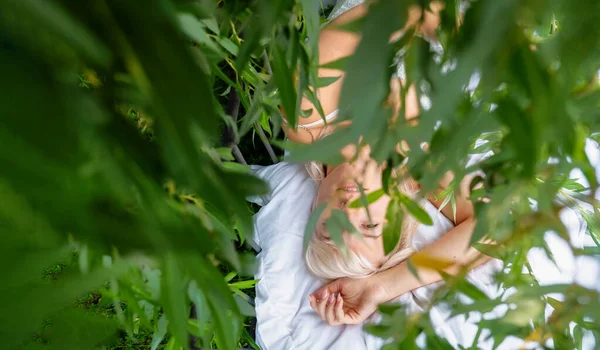 一个迷人的 年轻的 性感的金发女人 躺在绿树成荫的自然环境中 躺在一棵枯萎的柳树下 几乎完全被绿叶覆盖 她迷人的画像令人垂涎欲滴 — 图库照片