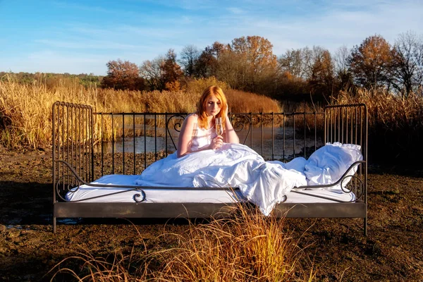 性感性感迷人的红头发女人躺在床上 喝着香槟酒 悠闲地享受着秋天橙色湖水的户外自然美景 — 图库照片