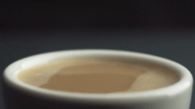 Kahve makinesinden siyah arka planda taze kahve dolu beyaz seramik bardağa düşen kahve damlasının yavaş çekim makrosu. Kremalı kahve. Bir düşüş yavaş çekimde zıplar 100 fps