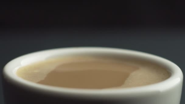 Slow motion macro shot of coffee drop falling from the coffee machine into white ceramic mug filled with fresh coffee on a black background. Crema on coffee. A drop bounces in slow motion 100fps — Stock Video