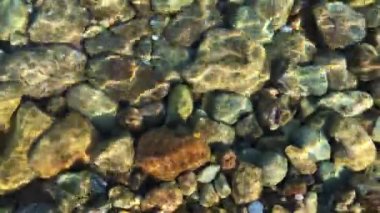 Nehir ya da denizin dibindeki çok renkli taş manzarası. Şeffaf berrak su. Çakıl taşlı deniz yatağı doğal arka plan. Denizin dalgaları, güneş ışınları. Su yakıcı arkaplan