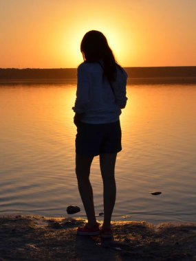 Bir kız, sarı bir günbatımının arka planında suya bakar ve düşünür ki...