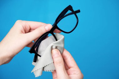 Kadının eli mavi arka planda mikrofiber bezle bardaklarını siliyor..