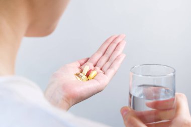 Elinde bir bardak su ve takviye kapsülü tutan kadın..