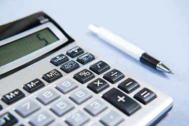 Mavi arkaplanda gri hesap makinesi ve beyaz kalem.