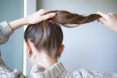 Genç bir kadın saçının çatlamış uçlarını tutuyor..