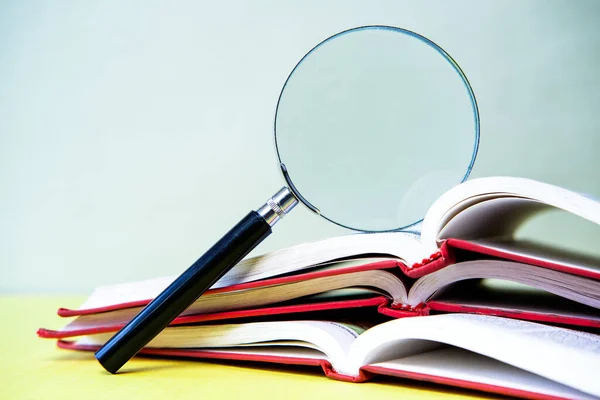 Büyüteç ve sarı zemin üzerine kitaplar.