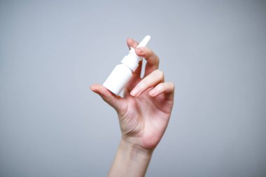 Burun spreyli beyaz bir şişe tutan bir kadın..