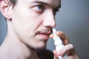 Genç adam burun akıntısı için burun spreyi kullanıyor..