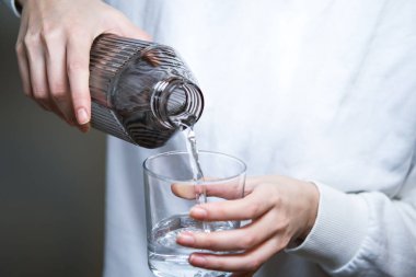 Bir kadının eli şeffaf bir bardağa su döküyor..