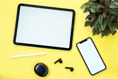 Beyaz ekranlı akıllı telefon ve dijital tablet, sarı arka planda kulaklık..