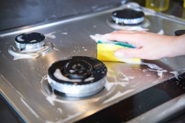 Bir kadının eli mutfakta modern bir gaz ocağını temizliyor..