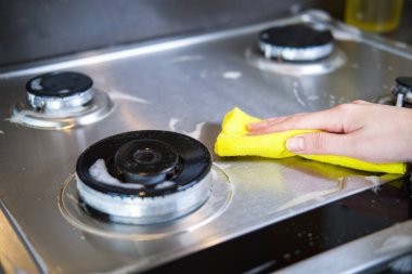 Bir kadının eli mutfakta modern bir gaz ocağını temizliyor..