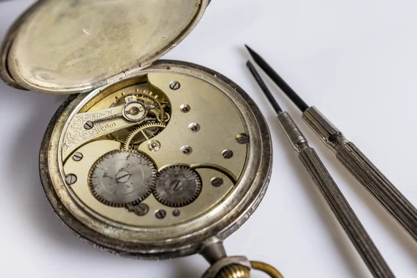 Antiques, vintage swiss pocket watch, two screwdrivers and tweezers lie on a white plastic table