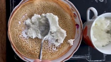 Bir adam peyniri ekşi kremayla krepin üzerine koyar ve onu bir tüpe sarar..