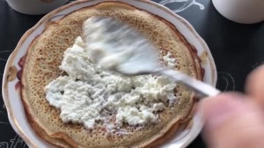 Bir adam peyniri ekşi kremayla krepin üzerine koyar ve onu bir tüpe sarar..