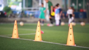 Turuncu işaret konisi için seçici odak noktası yeşil suni sahada futbol eğitim ekipmanları ve bulanık koçu ve çocuk futbolcuların eğitim geçmişi. Bulanık Spor arka planı.