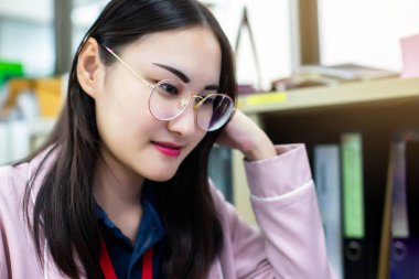 Gözlüklü gülümseyen Asyalı kadına seçici bir odak. Kameraya bakıyor. Mutlu Taylandlı öğrenci ya da çalışan ofiste poz veriyor..