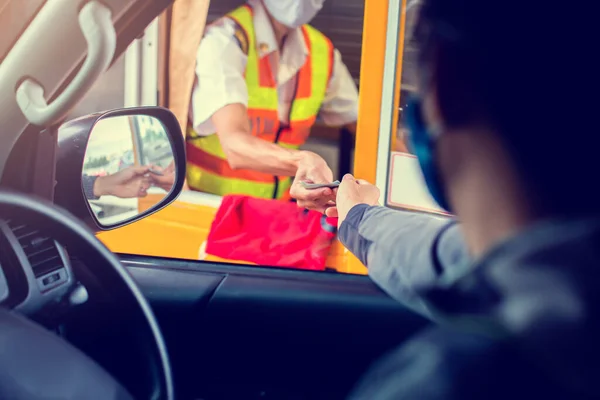 Selective focus to hand of driver pay for the expressway. Blurry image of drivers and cashiers wear face masks to prevent the spread of the Coronavirus (Covid-19). Pay expressway.