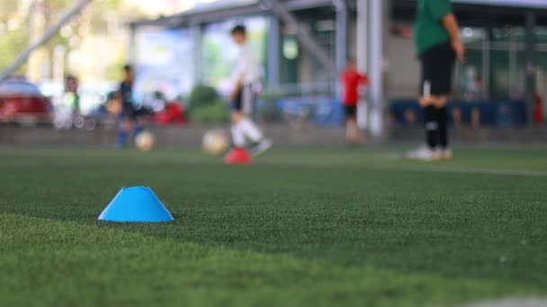 蓝锥标志和足球在绿色人工草地上的移动与模糊的少年足球队训练在足球学院 — 图库视频影像