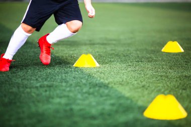 Bulanık çocuk futbolcuyla koni işaretleyicisine seçici odak yeşil yapay sahada koşuyor. Futbol akademisinin eğitim sınıfı için malzeme.