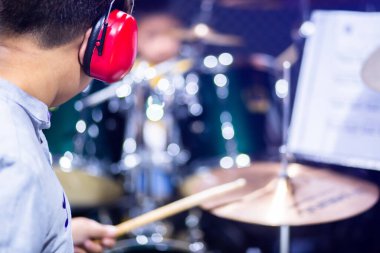 Müzik odasındaki oğlanı bulanıklaştıran davulcuların başında kırmızı kulaklık takmak. Öğretmen çocuğa bateri takımını ödemeyi öğretti. Müzik aleti konsepti.