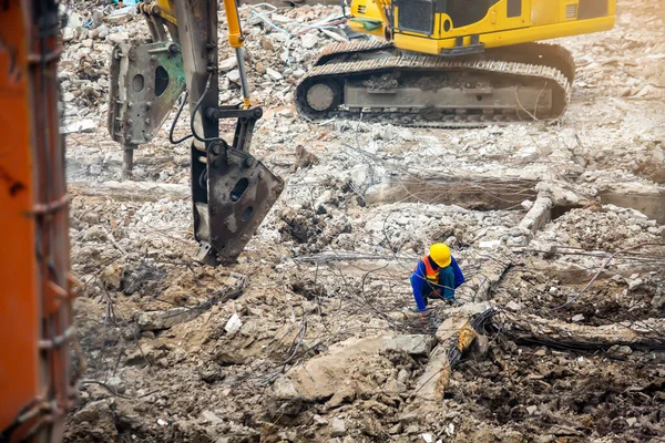 Construction workers sitting among the rubble of demolished buildings with working machines. Worker and demolition of a destroyed building.