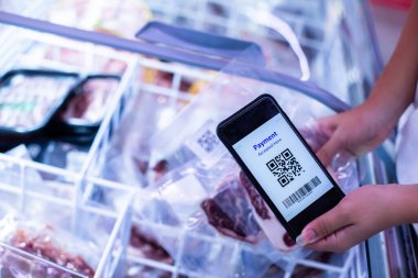 Süpermarkette dondurulmuş yiyeceklerle akıllı telefondaki QR kod etiketine seçici odak, bilgi ürünü ve çevrimiçi ödeme için QR kodunu tarayan müşteri.