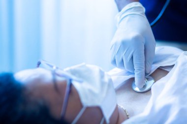 Doktorun eliyle seçici odak noktası steteskoplu Asyalı kadın hastayı muayene etmektir. Doktorlar ve hastalar Covid-19 virüsünü önlemek için maske takarlar. Sağlık ve Tıp Konsepti