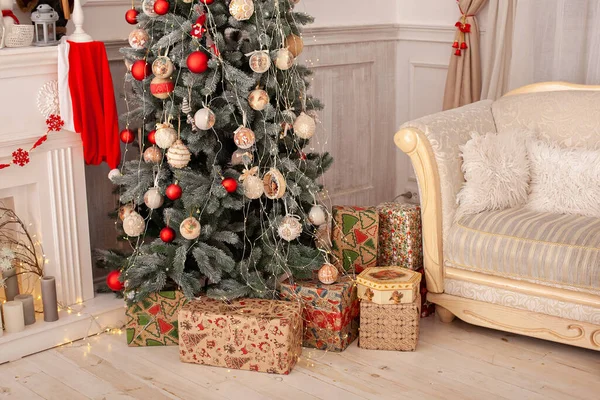 Decorated Christmas tree with gifts. Christmas tree decorated with toys, balls and lights glowing garlands. Cozy xmas interior room with sofa and Christmas tree. Scandinavian style living room