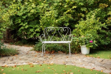Yaz bahçesinde dinlenmek için beyaz bir bank. Arka bahçedeki saksıda ortanca çiçekleri. Klasik dekoratif işlenmiş demir bahçe tezgahı. Samimi bahçe köşesi. Saksıda yeşil bitkiler olan evin içi.. 
